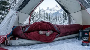 Interior of a winter tent showing a burgundy fleece blanket layered over a sleeping bag for extra thermal insulation in Canadian sub-zero weather.