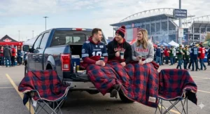 A 4K photorealistic image of Canadian football fans tailgating in a stadium parking lot, comfortably wrapped under a large, heavily insulated oversized outdoor blanket.
