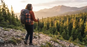 A hiker carrying a compact, lightweight packable camping blanket attached to their backpack during a trek.