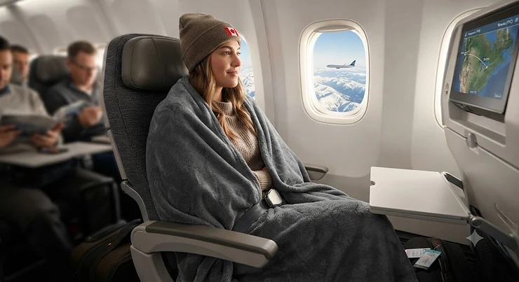A traveller wrapped in a cozy airline travel blanket while seated on a flight to a Canadian destination.