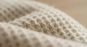 Macro detail shot showing the soft, breathable thermal weave of a cream-coloured cashmere-blend travel blanket scarf combo