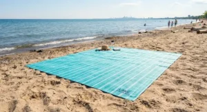 Sand-free quick dry beach blanket spread out on the shores of Lake Ontario on a sunny afternoon.